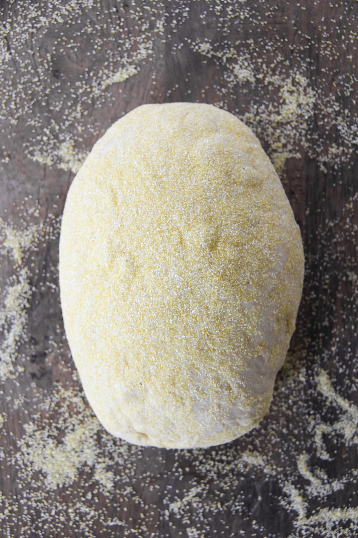 a loaf of bread dough sits on a sprinkling of cornmeal on a table