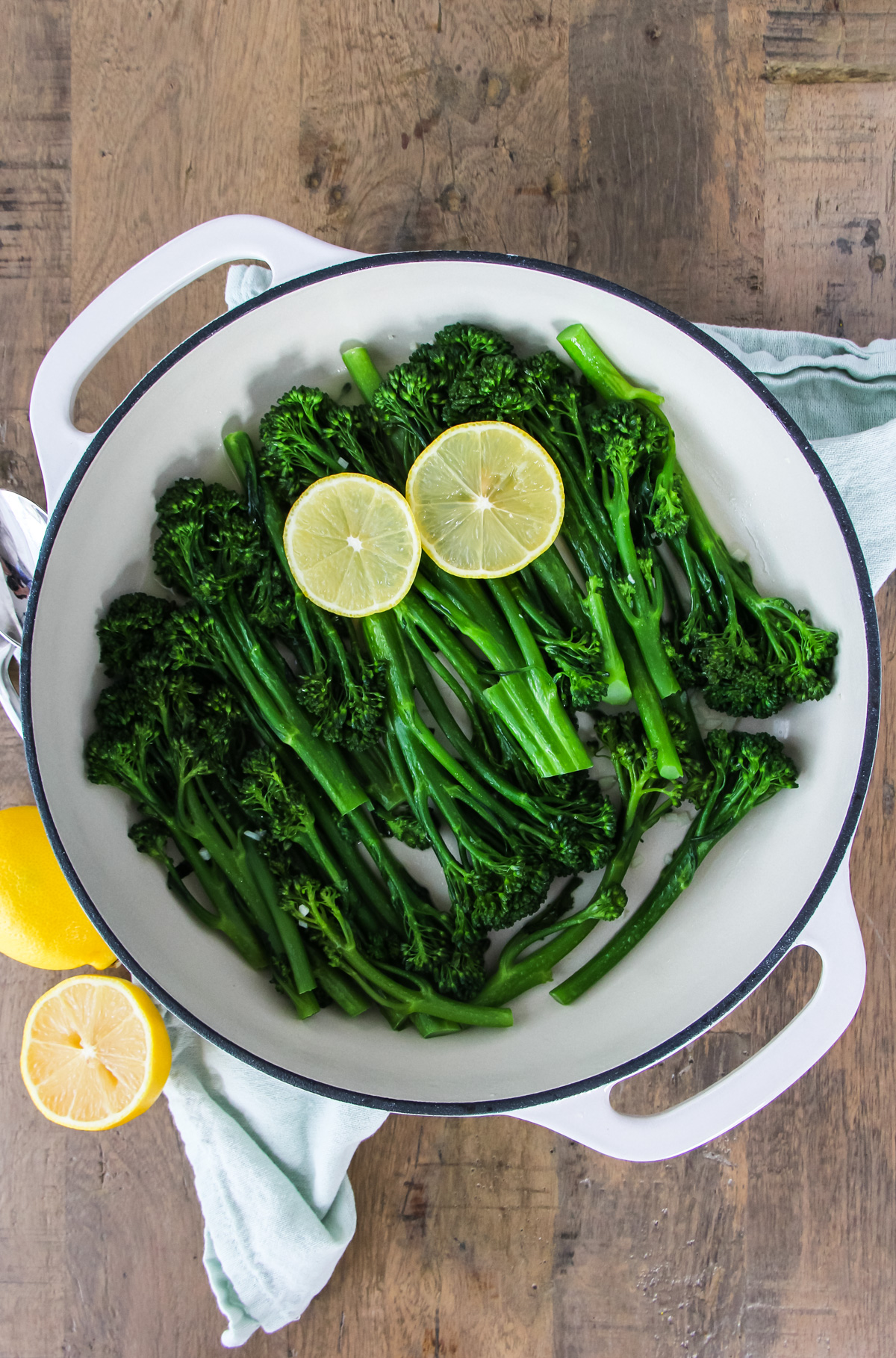 a top down close up of a pan of lemon garlic broccolini. two slices of lemon rest on the broccolini.