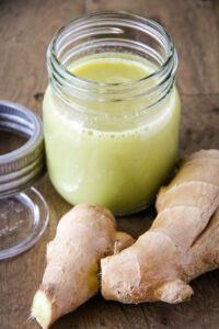 a jar of fresh ginger juice. a fresh root sits in the foreground
