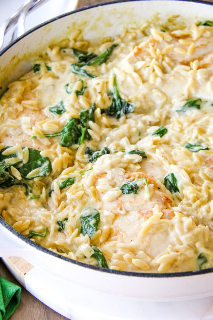 a close up image of a dish of creamy chicken orzo with spinach