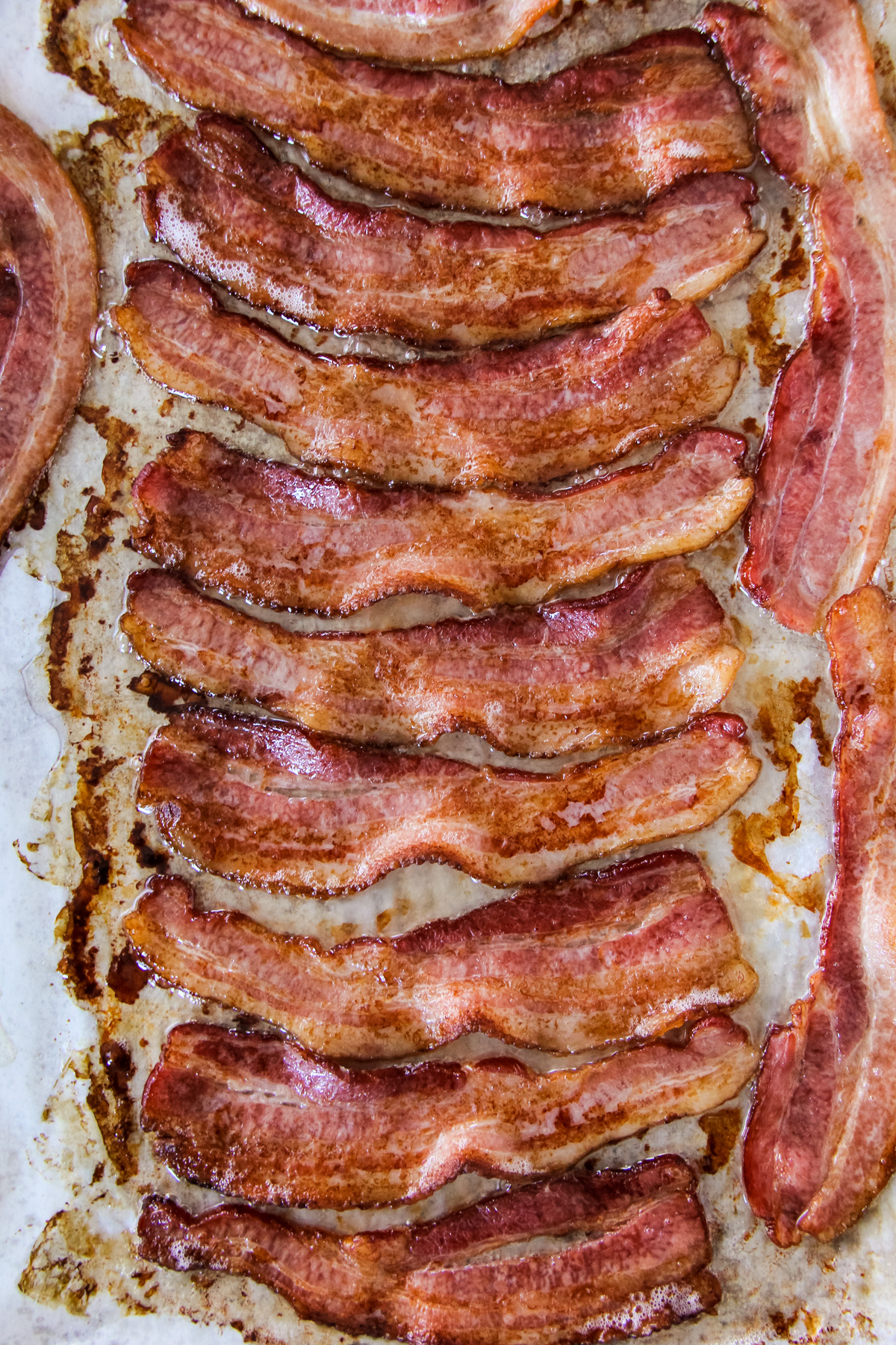 a top down close up image of a baking tray filled with cooked bacon
