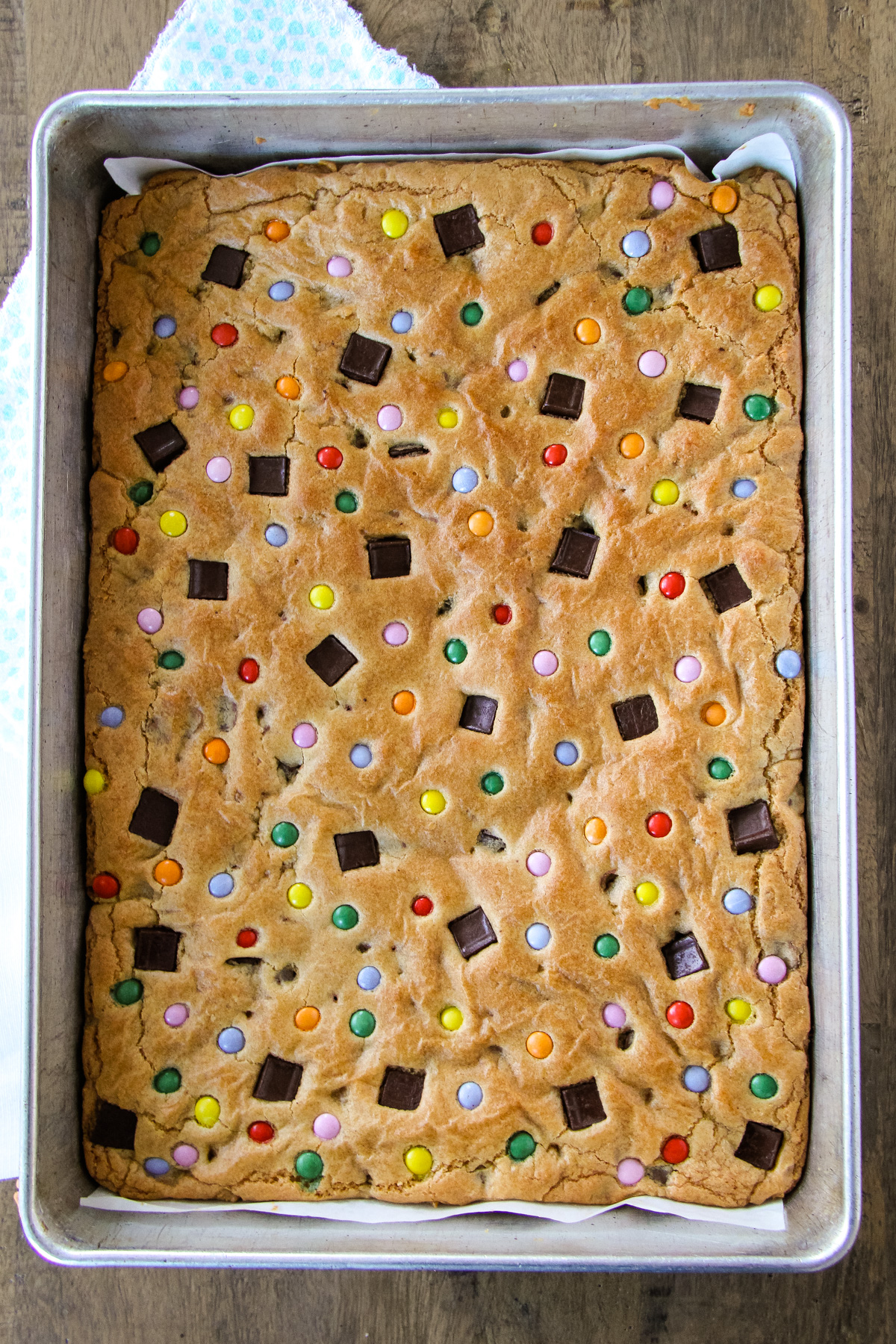 a top down image of chocolate chip cookie bars dotted with coloured candy, in a baking pan
