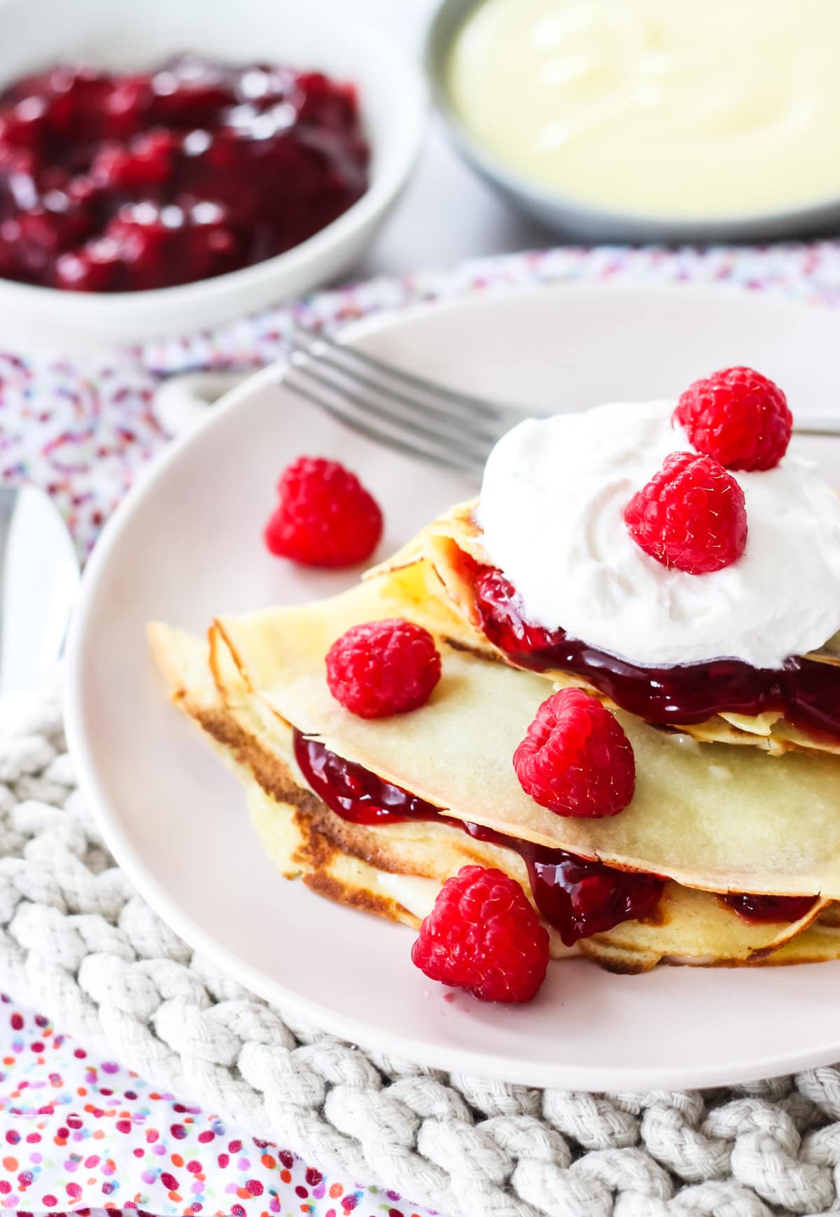 raspberry creme crepes topped with whipped cream and fresh raspberries on a plate with a fork