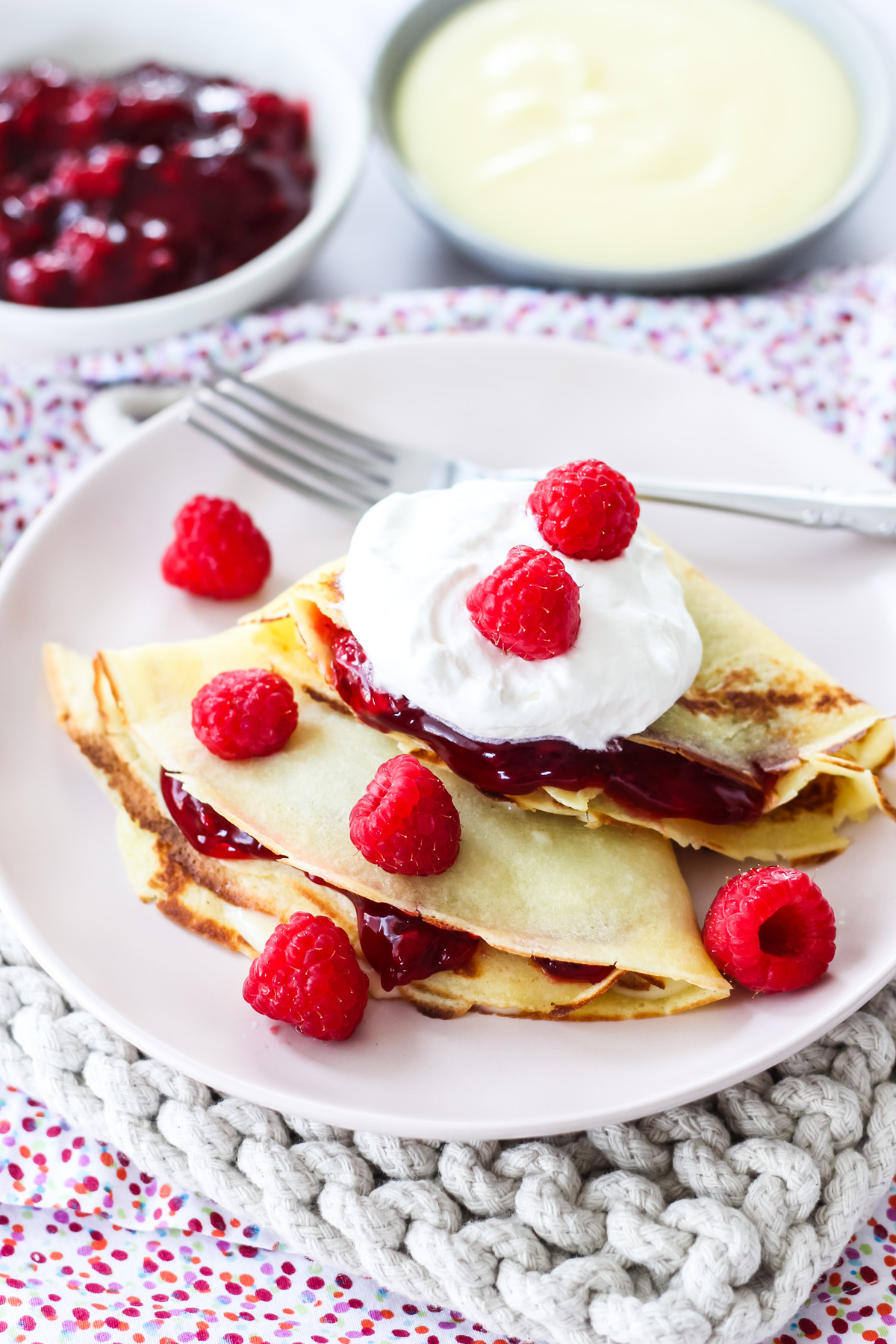 raspberry creme crepes topped with whipped cream and fresh raspberries on a plate with a fork