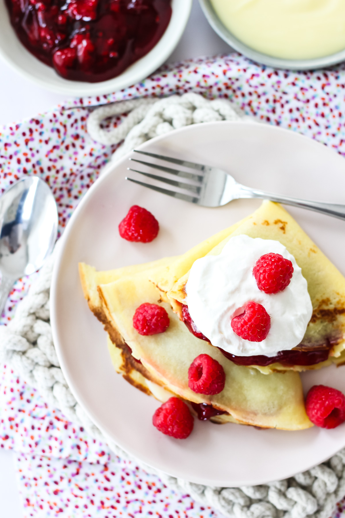 a top down picture of raspberry creme crepes topped with whipped cream and fresh raspberries