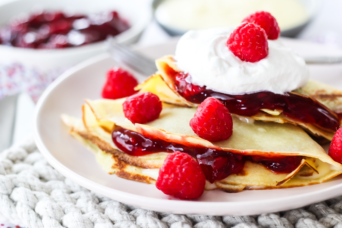 a close up of raspberry creme crepes topped with whipped cream and fresh raspberries