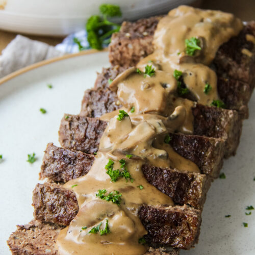 a plate filled with sliced beef stroganoff meatloaf smothered in gravy