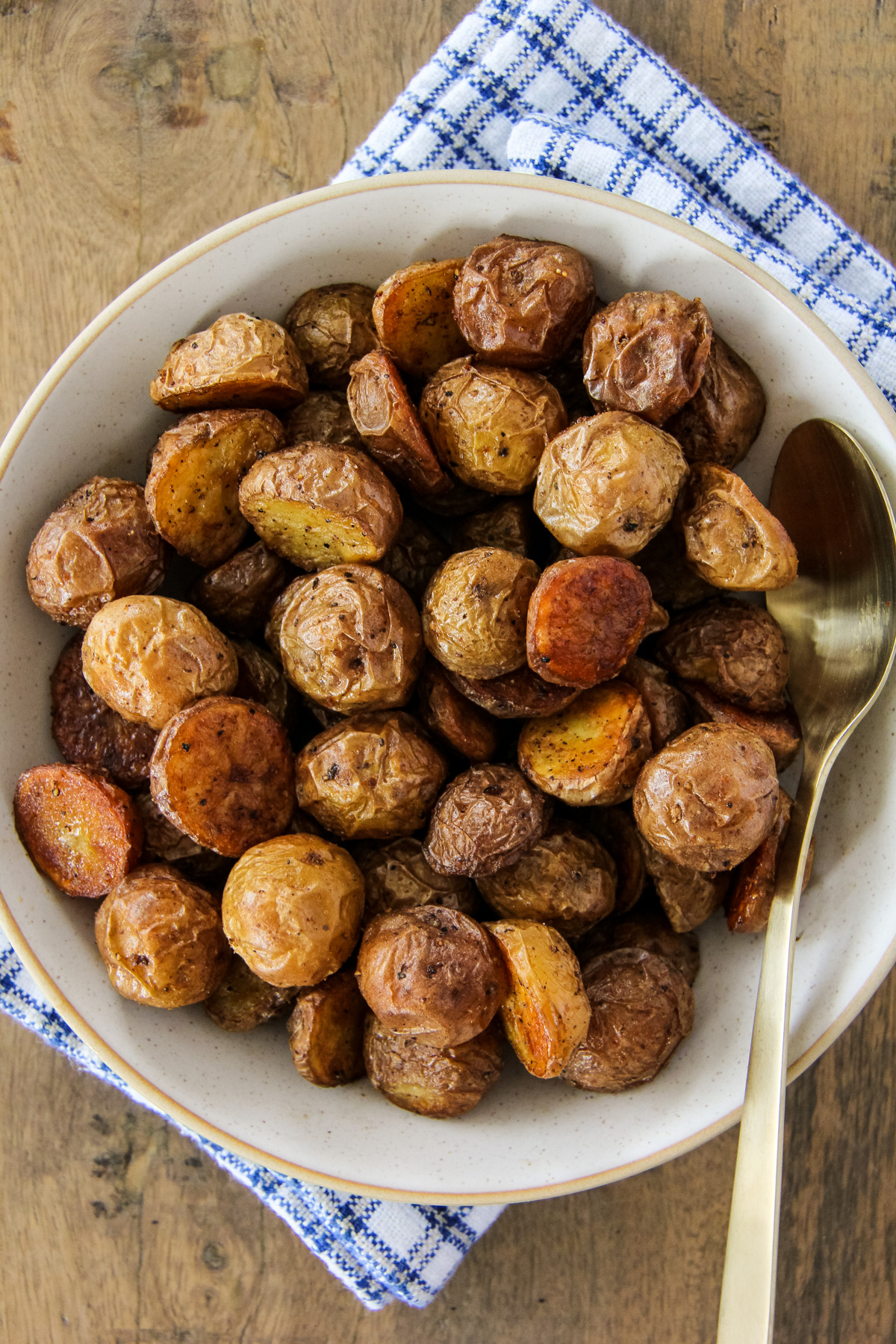 a top down image of a bowl filled with oven roasted potatoes and a spoon