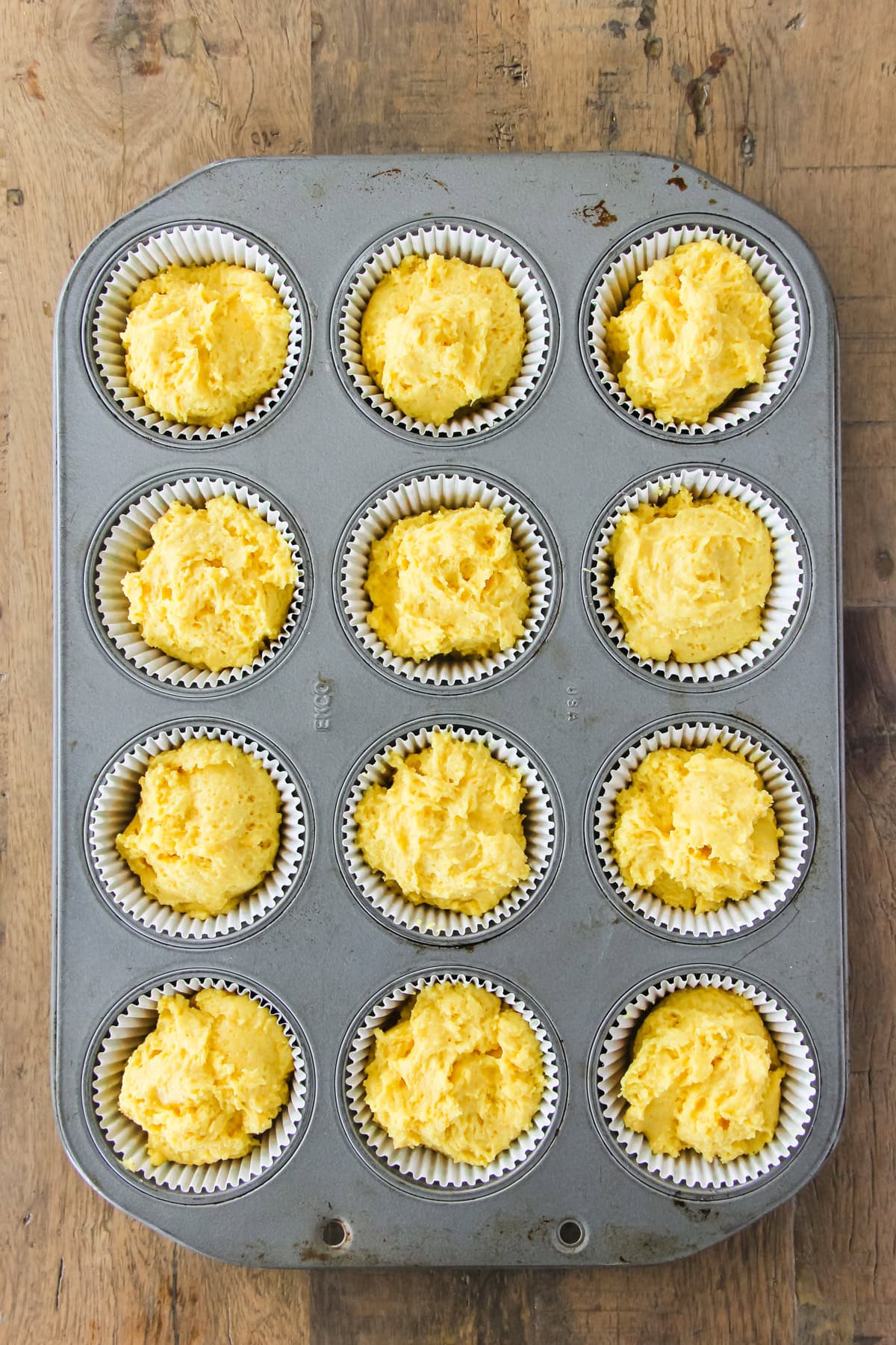 a top down view of a muffin tin filled with orange blender muffin batter