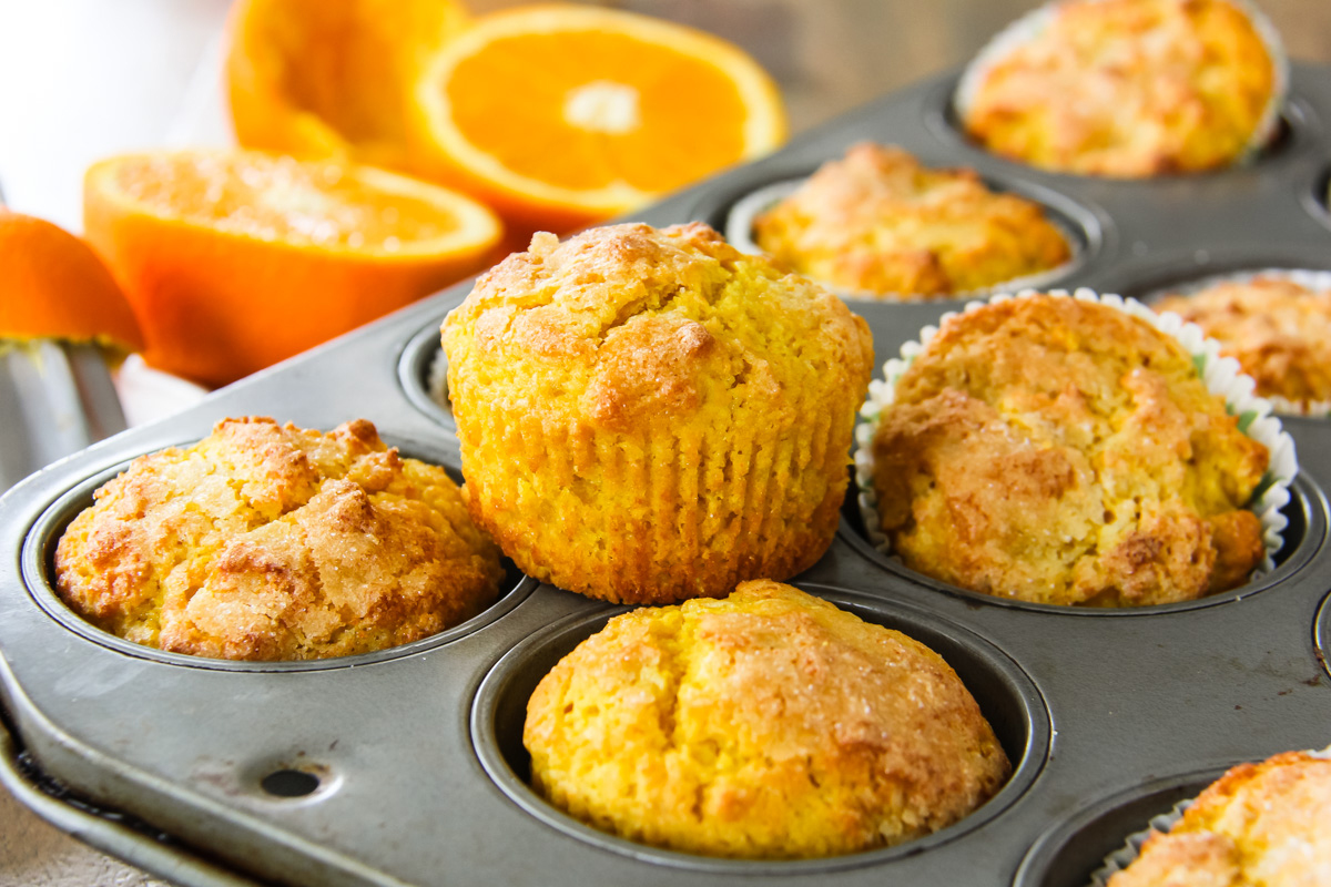 an orange blender muffin sitting on a muffin tray. in the background are two orange halves