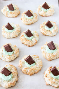 a baking tray of coconut macaroons with green frosting and a chocolate mint in the centres