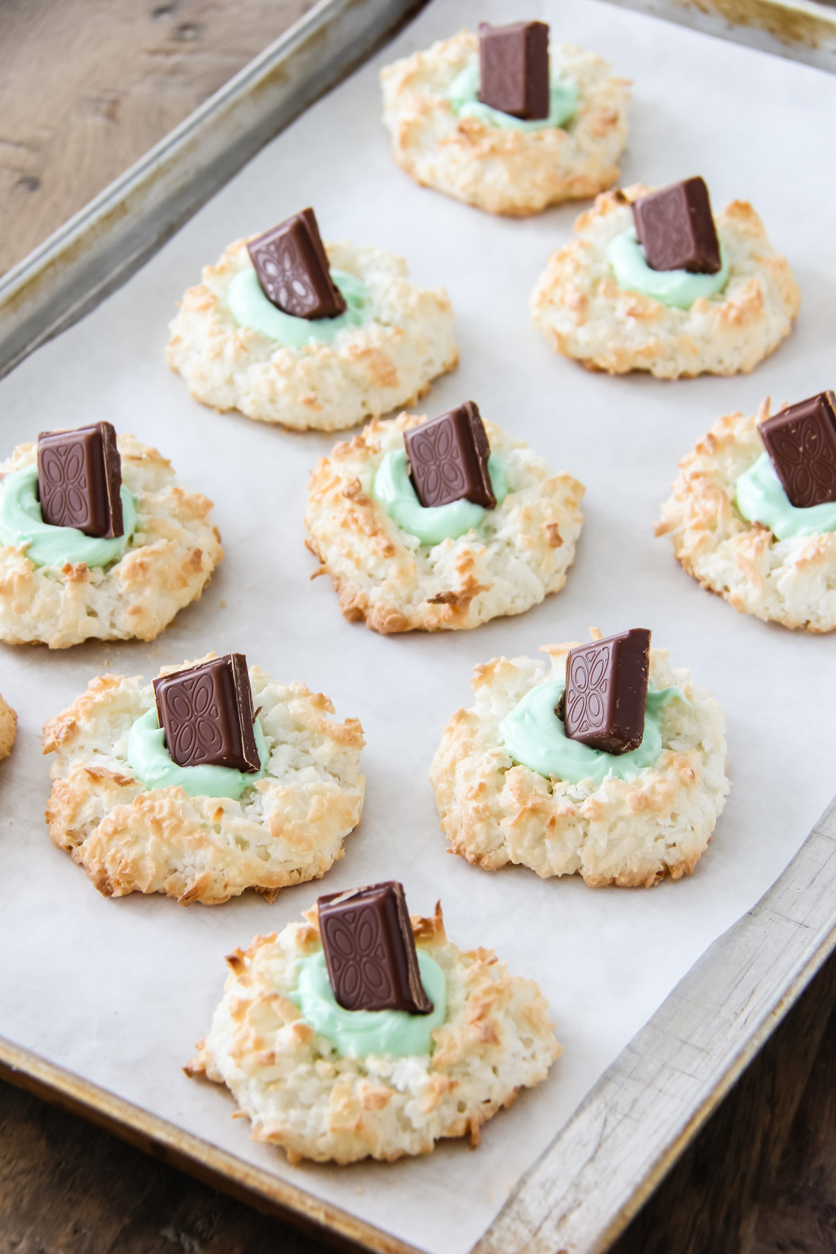 a baking tray of coconut macaroons with green frosting and a chocolate mint in the centres