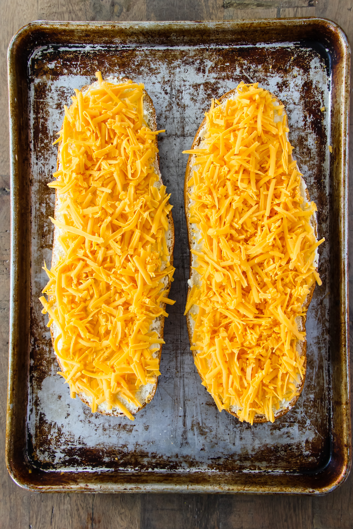 two halves of French bread covered in shredded cheddar cheese are placed on a baking sheet