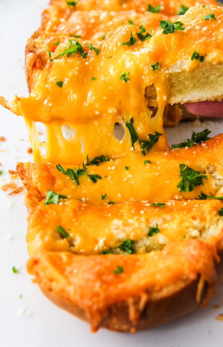 a piece of cheesy garlic bread is being pulled away from the baked loaf