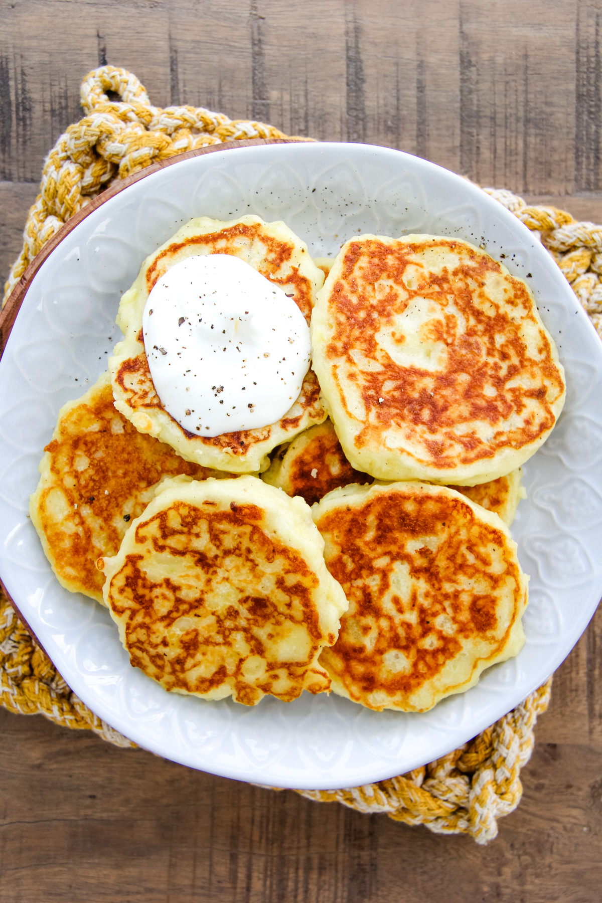 a top down image of a plate of mashed potato pancakes with a dollop of sour cream