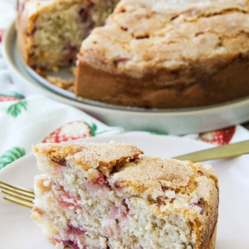 a slice of Strawberry Buttermilk Cake sits on a plate next to the cake