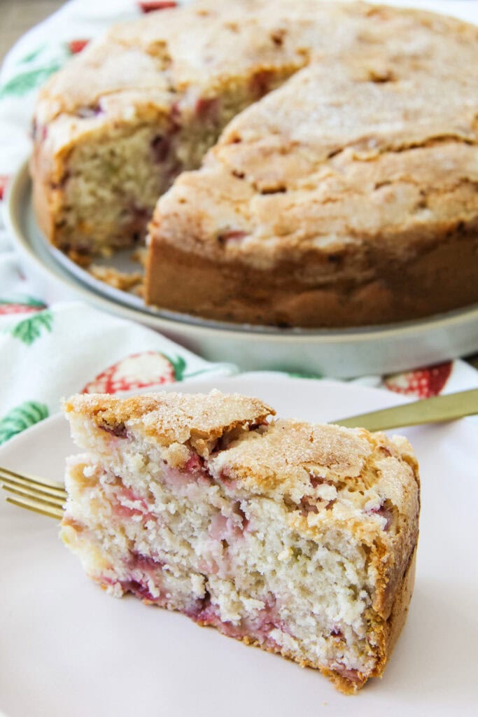 a slice of Strawberry Buttermilk Cake sits on a plate next to the cake