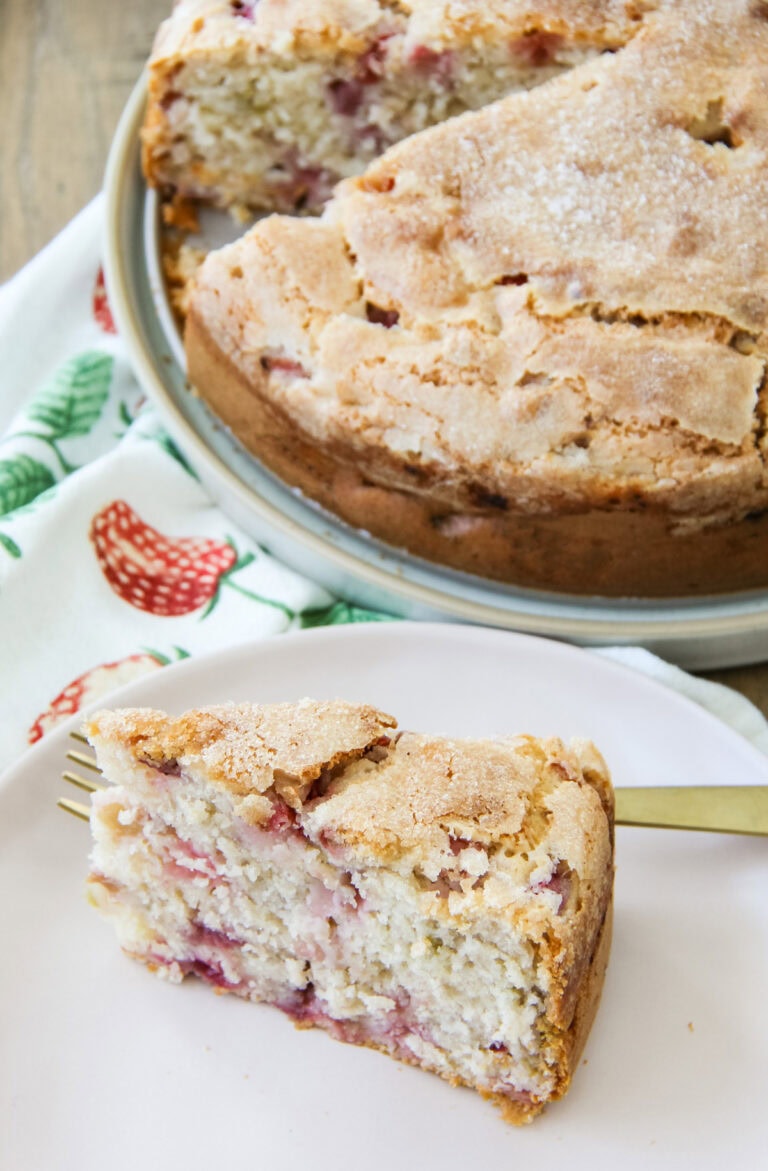 a slice of Strawberry Buttermilk Cake sits on a plate next to the cake