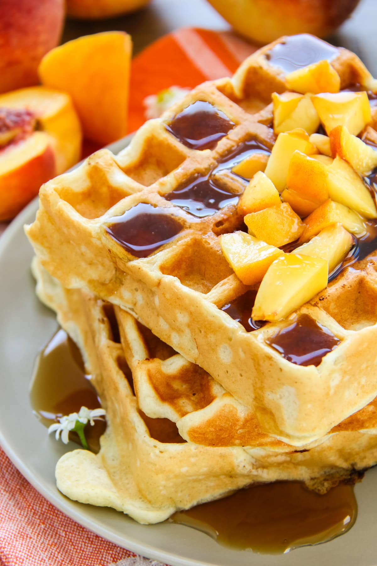 a stack of peach waffles with chopped fresh peaches and syrup