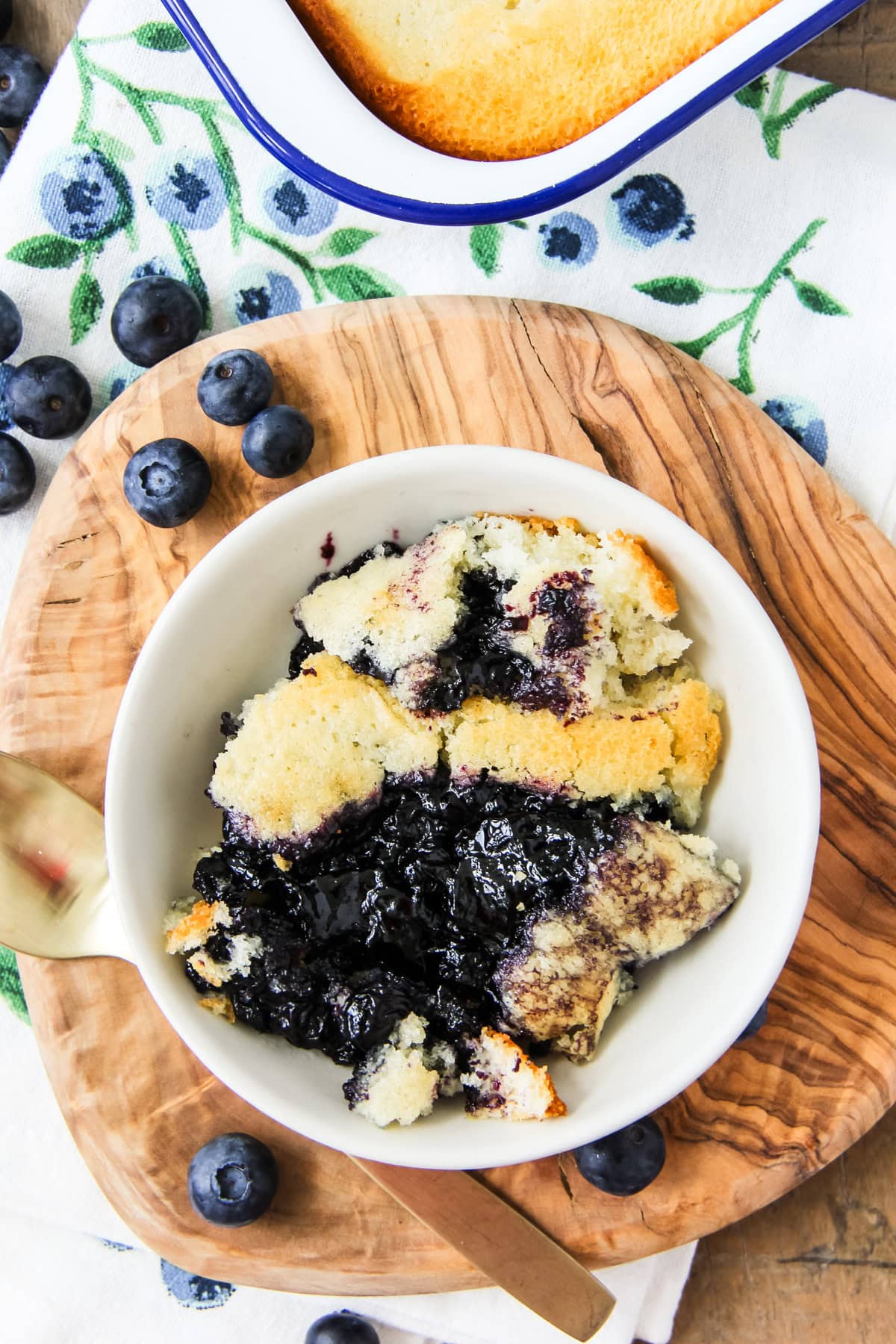 a scoop of blueberry pudding cake in a white bowl sitting on a wooden board