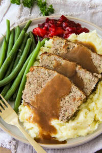 a dinner plate filled with Turkey and Stuffing Meatloaf, mashed potatoes, green beans and cranberry sauce