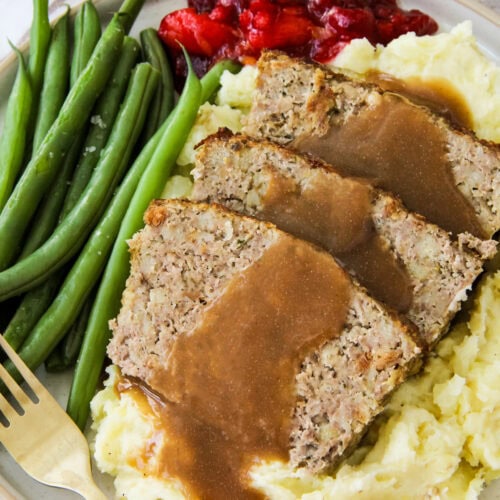 a dinner plate filled with Turkey and Stuffing Meatloaf, mashed potatoes, green beans and cranberry sauce