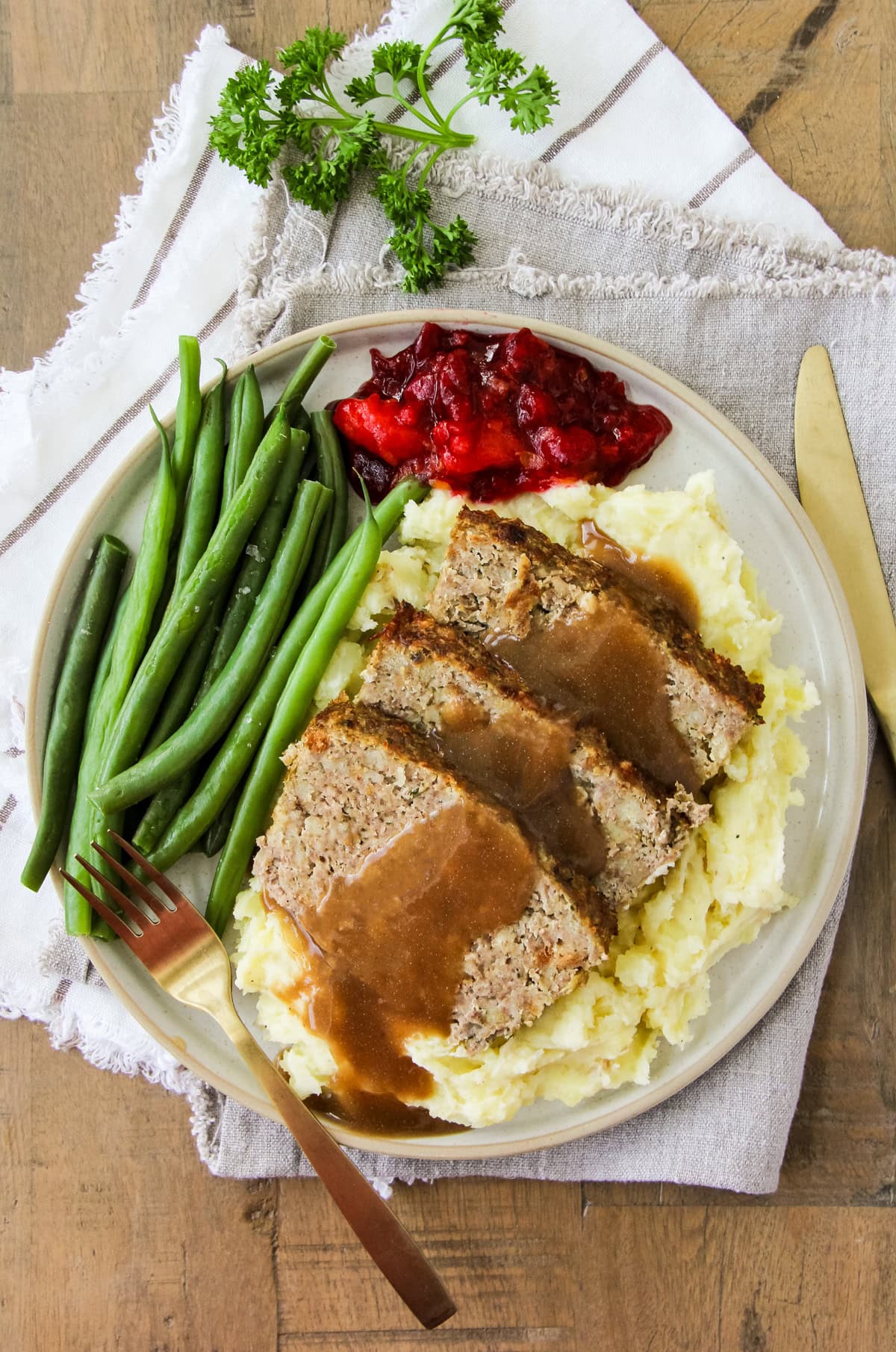 a dinner plate filled with Turkey and Stuffing Meatloaf, mashed potatoes, green beans and cranberry sauce